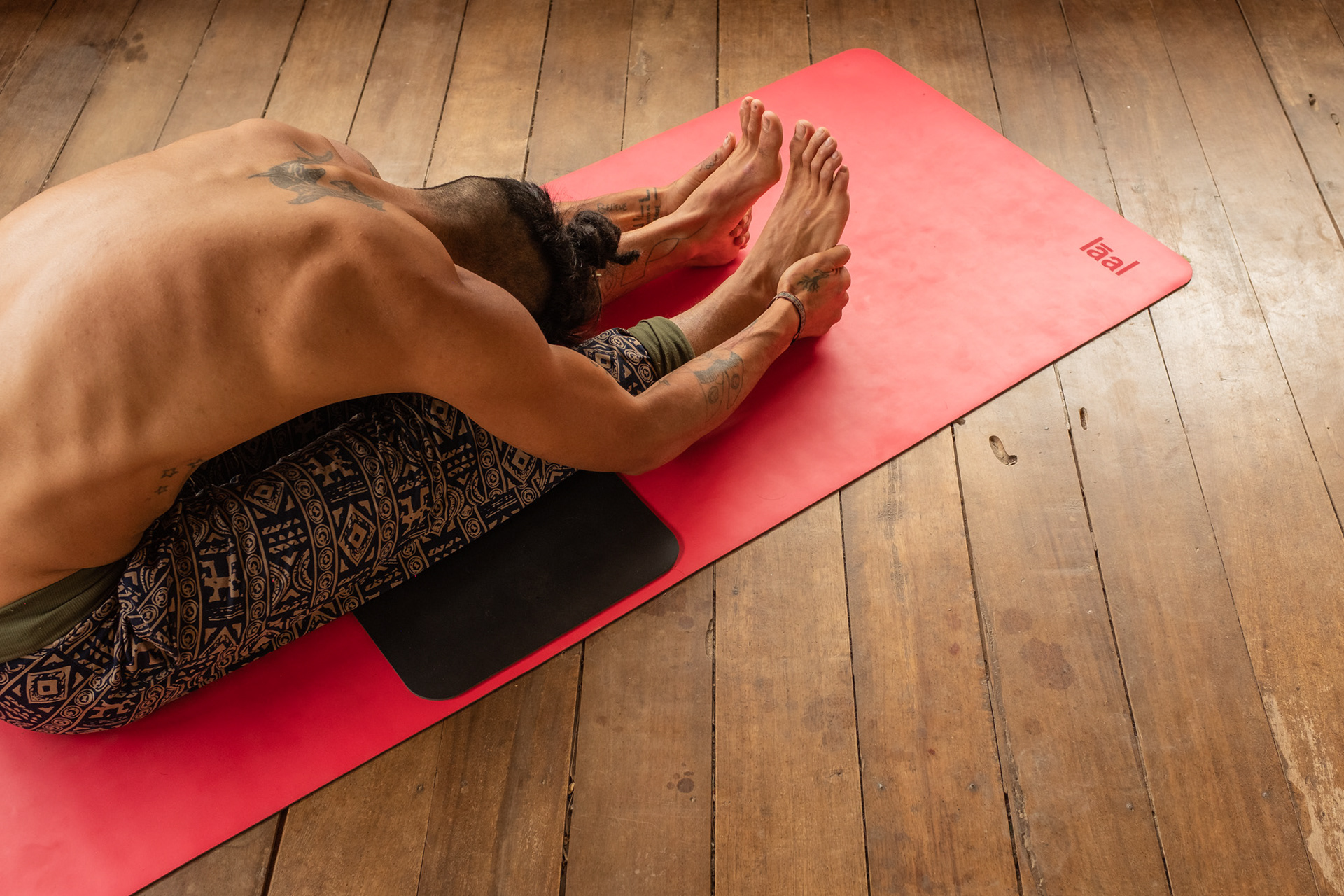 Persona tumbada boca abajo sobre una esterilla roja en una postura de yoga restaurativo