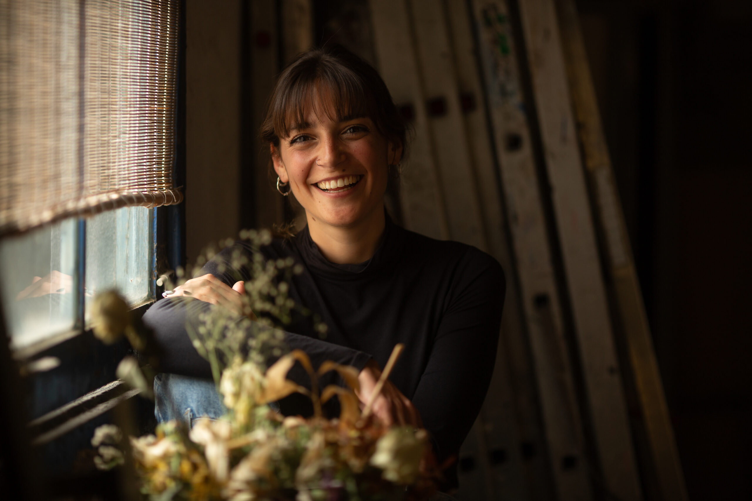Mujer junto a una ventana rodeada de ramos de flores secas
