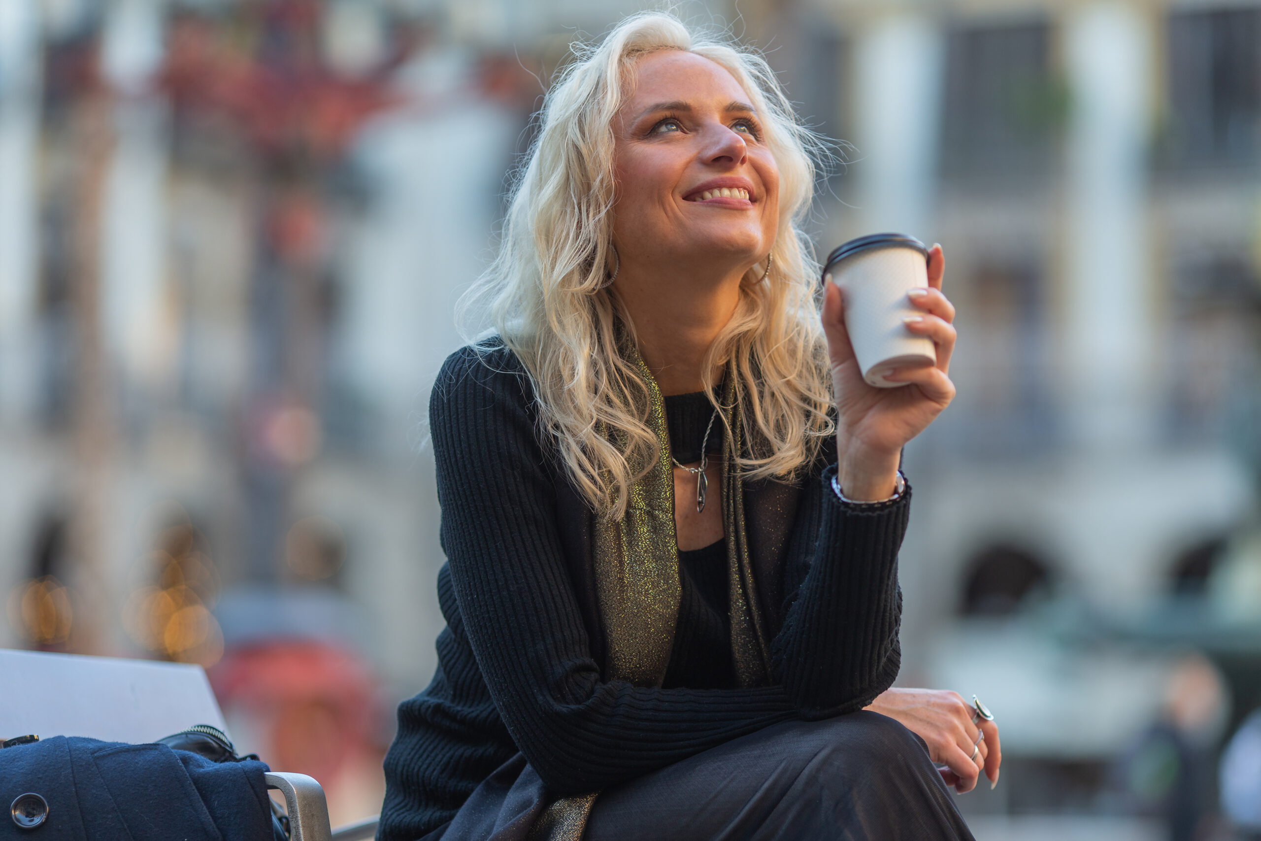 Mujer rubia sentada al aire libre con un vaso de café en la mano