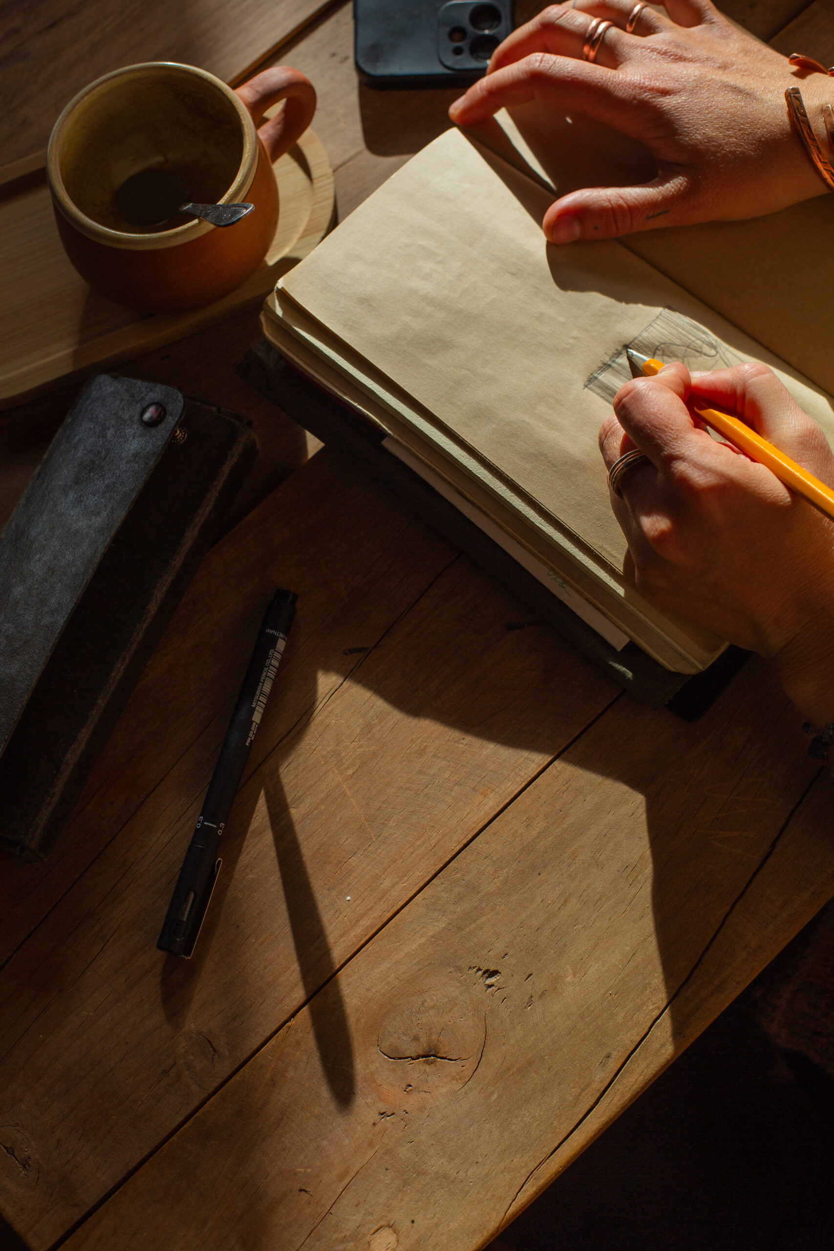 Manos escribiendo en un cuaderno junto a una taza de café sobre una mesa de madera