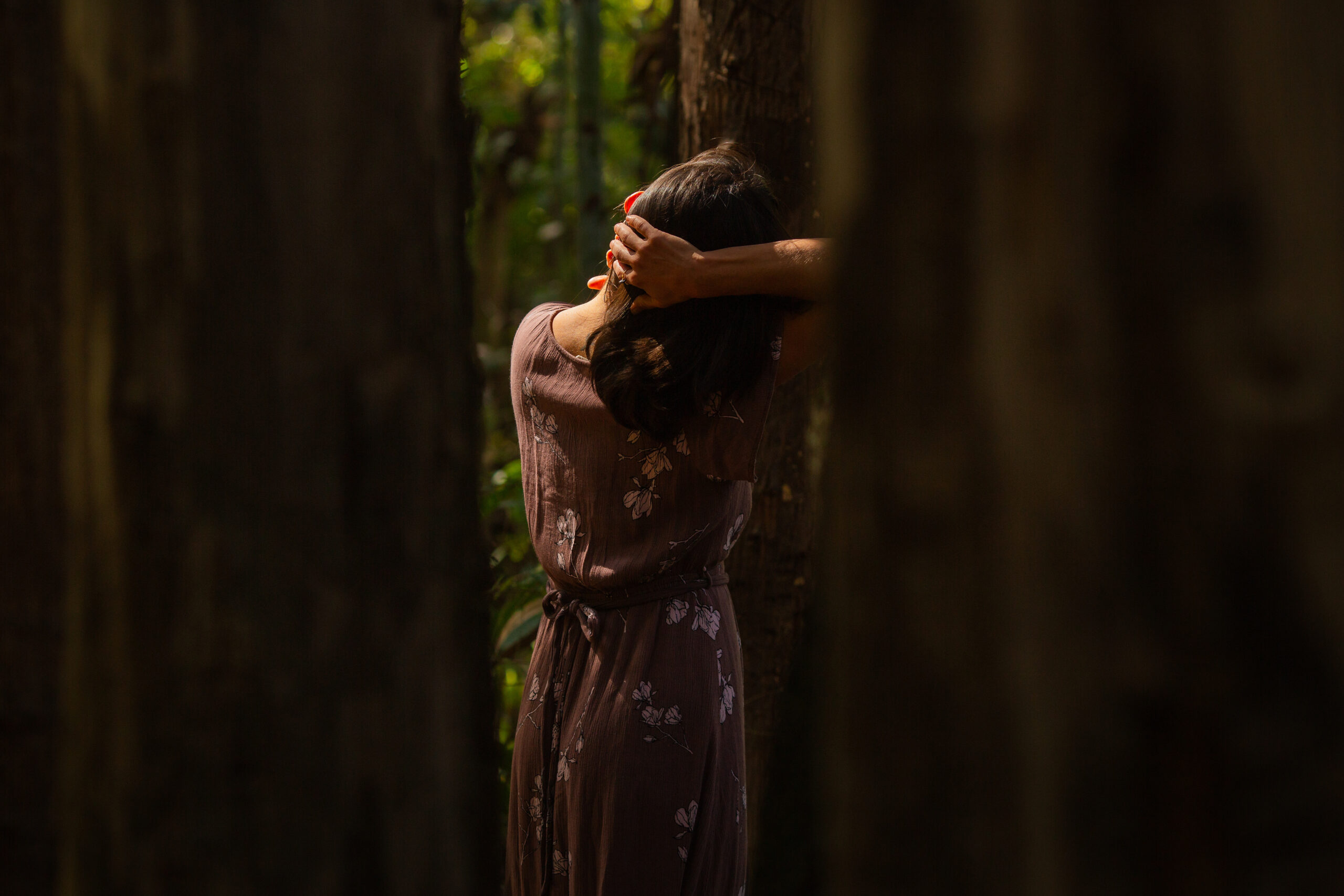 Mujer con vestido claro apoyada en un árbol en un bosque en penumbra