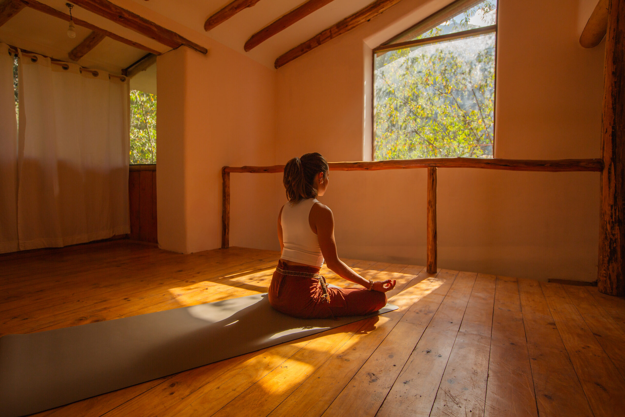Mujer sentada en meditación en una sala de madera con la luz entrando por la ventana