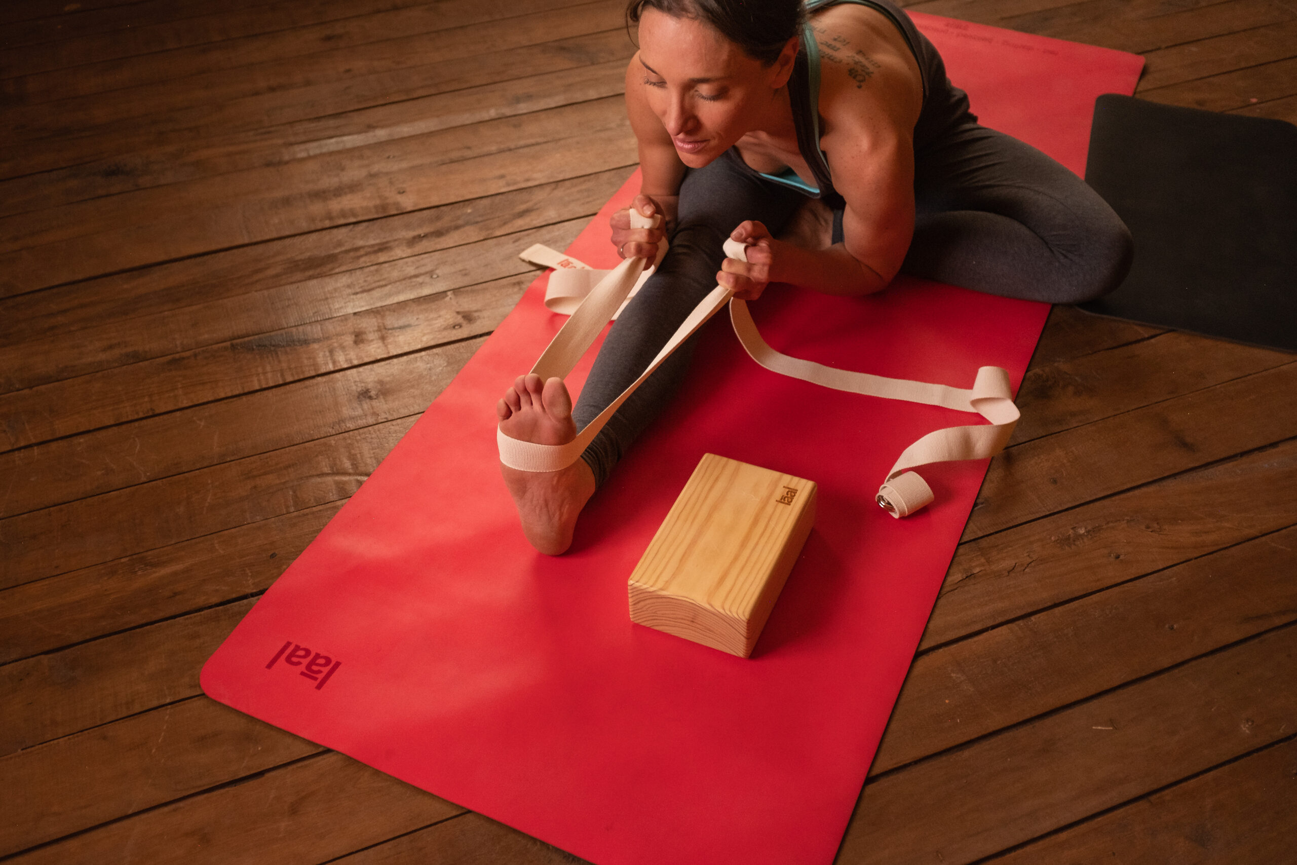 Mujer usando una cinta y un bloque de yoga sobre una esterilla roja